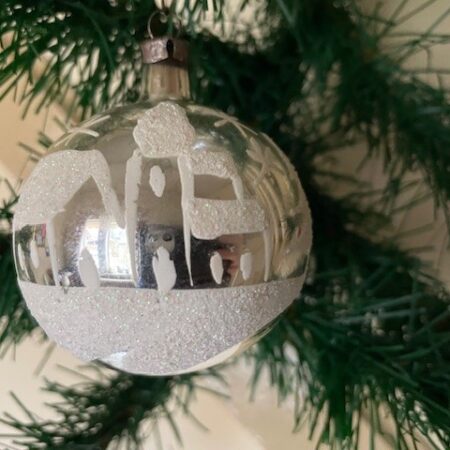 Oude kerstbal van dun geblazen glas gedecoreerd met een voorstelling onder een sterrenhemel van van kerstbomen huis en kerk