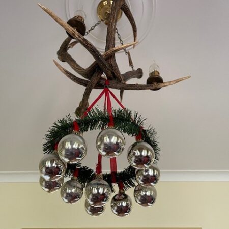 Oude, retro adventskrans van plastic en rood chenille waaraan kerstballen van dun geblazen glas in zilver