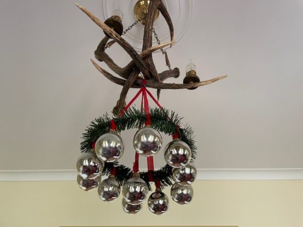 Oude, retro adventskrans van plastic en rood chenille waaraan kerstballen van dun geblazen glas in zilver